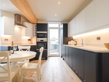 A kitchen with black and white cabinets a round white table with chairs and a glass door at Ferryside in Kingswear