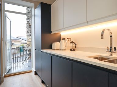 A kitchen with black cabinets white countertop white kettle toaster and coffee press and an open door leading outside at Ferryside in Kingswear