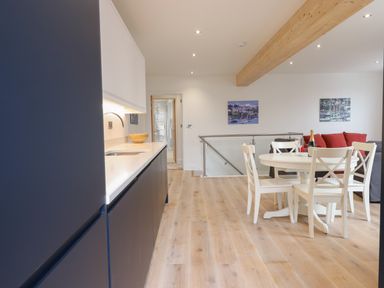 A kitchen with dark cabinets and a white countertop next to a dining area with a round table and white chairs at Ferryside in Kingswear