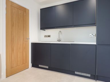 A kitchen with dark cabinets a sink a wooden door and tiled floor at Ferryside in Kingswear
