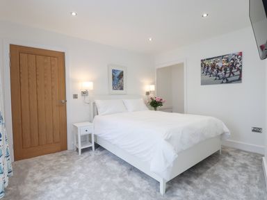 A bedroom with a white bed two wall-mounted lamps a wooden door and pictures on the wall at Ferryside in Kingswear