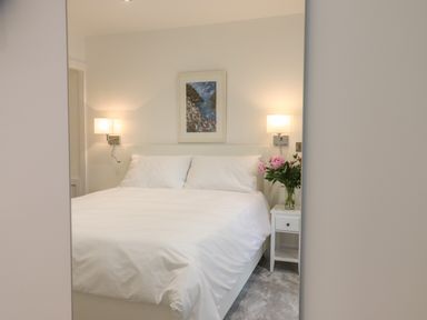 A bedroom with a white bed and pillows bedside table with flowers and wall lamps at Ferryside in Kingswear