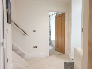 A hallway with stairs on the left and an open wooden door leading to a room with curtains at Ferryside in Kingswear