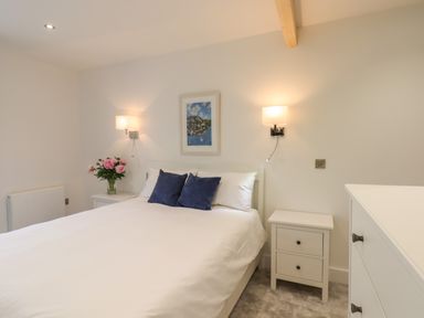A bedroom with a bed and pillows two bedside tables with lamps and flowers a chest of drawers and a framed picture on the wall at Ferryside in Kingswear