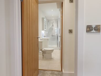 A view through a wooden door into a bathroom with a toilet sink and shower at Ferryside Kingswear