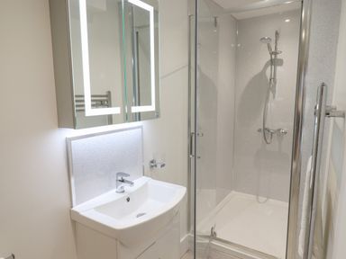 A bathroom with a sink basin under an illuminated mirror and a glass shower enclosure at Ferryside in Kingswear