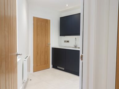 A small room with a wooden door a radiator and black cabinets with a sink at Ferryside in Kingswear