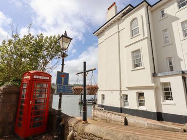 A red telephone box next to a lamp post and a no parking sign beside a white building by the water at Ferryside in Kingswear