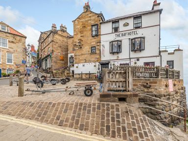 A cobblestone street with fishing trailers and a white building named The Bay Hotel at The Shepherd's Rest in Robin Hood's Bay