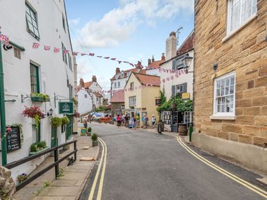 A street with white and stone buildings and hanging flower baskets at The Shepherd's Rest in Robin Hood's Bay