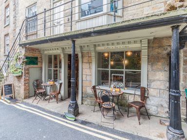Outdoor seating area with small tables and metal chairs outside a cafe with signage for coffee tea and cakes at The Shepherds Rest in Robin Hoods Bay