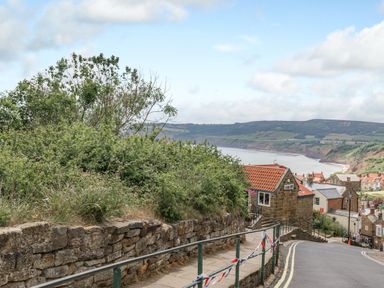 A coastal village street with stone wall railings and houses overlooking a bay