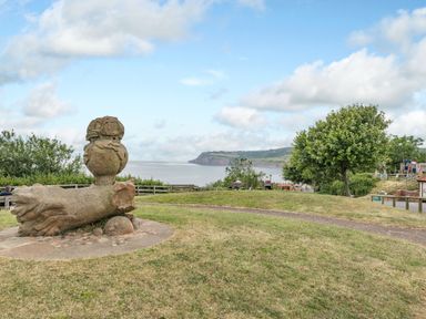 A grassy park area with a stone sculpture and a coastal view at The Shepherds Rest in Robin Hoods Bay