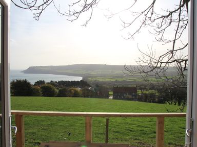 A view of green fields and distant coastline seen through an open door with a wooden railing at The Shepherds Rest in Robin Hoods Bay