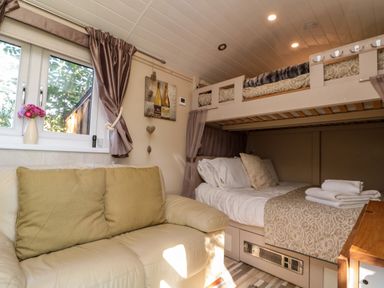 A room with a cream leather sofa with cushions a bunk bed with folded towels and bedding and a window with curtains at The Shepherd's Rest in Robin Hood's Bay