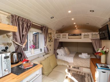 A compact living area with a sofa, kitchenette, bed, bunk above, and a wall-mounted TV at The Shepherd's Rest in Robin Hood's Bay