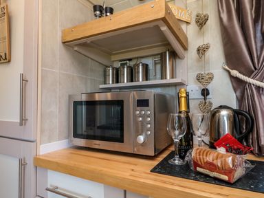 A kitchen countertop with a microwave oven a kettle two wine glasses a bottle of prosecco and a package of tea biscuits at The Shepherd's Rest in Robin Hood's Bay