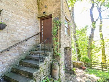 Stone steps with metal railings leading to a wooden door on a stone building surrounded by trees and plants at Keepers in Nenthead near Alston