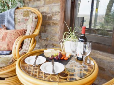 A glass table with plates cutlery wine glasses wine and a plant next to a cushioned chair at Keepers in Nenthead near Alston
