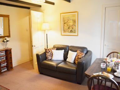 A living room with a black leather sofa and cushions a dining table with food and drinks and a wooden cabinet with DVDs at Keepers in Nenthead near Alston