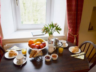 A breakfast table with croissants cups of tea fruit bowl toast jam and juice at Keepers Nenthead near Alston