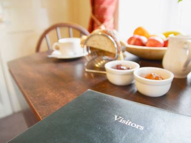 A wooden table with a visitors book jam pots a cup of tea bread in a rack and a bowl of fruit at Keepers in Nenthead near Alston