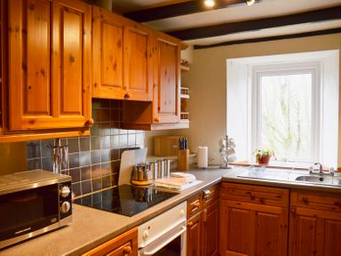 A kitchen with wooden cabinets a microwave stove a window with a plant and a sink at Keepers Nenthead near Alston