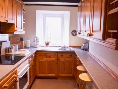 A kitchen with wooden cabinets a countertop a sink a window and two stools at Keepers in Nenthead near Alston