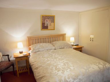 A bedroom with a double bed, two bedside tables with lamps, a framed picture on the wall, a chair, and a built-in wardrobe at Keepers in Nenthead near Alston