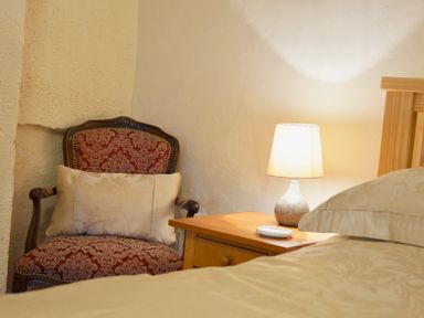 A bedroom corner with a patterned armchair a wooden nightstand with a lamp and part of a bed at Keepers in Nenthead near Alston