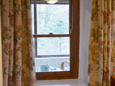 A window with floral curtains looking out to a tree and a table with a plant at Keepers in Nenthead near Alston
