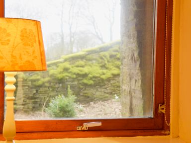 A window with a stone wall and greenery outside and a lamp with an orange shade inside at Keepers in Nenthead near Alston