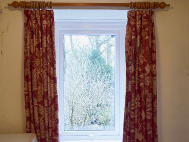 A window with floral patterned curtains and a view of trees outside at Keepers in Nenthead near Alston