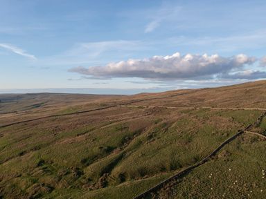 A rural landscape with grass fields and fenced areas under a blue sky with clouds at Keepers in Nenthead near Alston