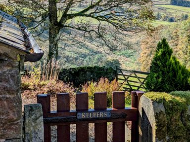 A wooden garden gate with a sign saying Keepers opening to a countryside view with trees and a wooden fence at Keepers in Nenthead near Alston