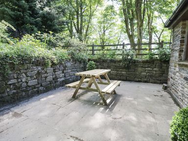 An outdoor patio with a wooden picnic table surrounded by stone walls and greenery at Bothy in Nenthall near Alston