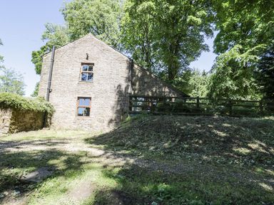 Stone building with two windows surrounded by trees and a wooden fence at Bothy Nenthall near Alston
