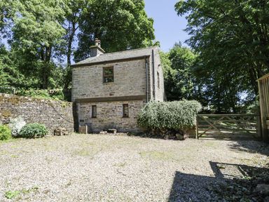 A stone house with small windows surrounded by trees and a gravel yard at Bothy Nenthall near Alston