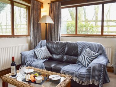 A living room with a leather sofa covered with a striped blanket and cushions next to a glass table with wine and snacks at Bothy Nenthall near Alston