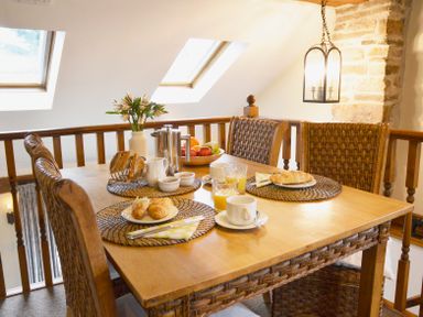 A dining table set with croissants, juice, coffee, and flowers near skylights at Bothy in Nenthall near Alston