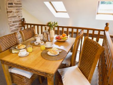A dining area with a wooden table set with cups, glasses of orange juice, croissants, a fruit bowl, and a vase with flowers at Bothy in Nenthall near Alston