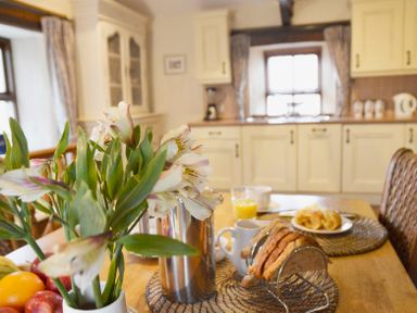 A kitchen with flowers and fruit on a table with bread juice and crockery at Bothy in Nenthall near Alston