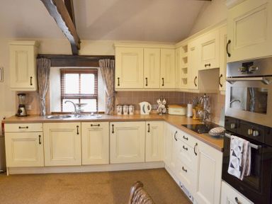 A kitchen with cream cabinets brown countertops and a window with blinds at Bothy in Nenthall near Alston