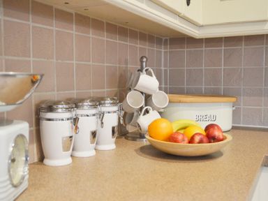 A kitchen counter with a fruit bowl cups on a holder canisters and a bread box at Bothy Nenthall near Alston