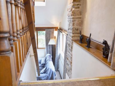 A narrow stairway leading down to a room with a sofa covered in striped fabric a window with curtains and a wall with three cat figurines on a wooden shelf at Bothy Nenthall near Alston