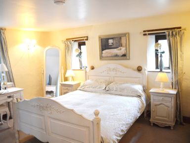A bedroom with a bed a mirror bedside tables with lamps and floral curtains at Bothy in Nenthall near Alston