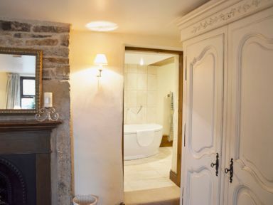 A room with a white cabinet a fireplace with a mirror and a lamp on the wall next to a bathroom with a bathtub at Bothy Nenthall near Alston