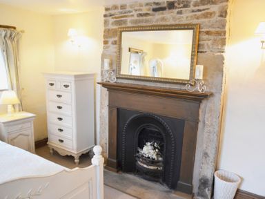 A bedroom with a fireplace mirror chest of drawers and bedside table at Bothy Nenthall near Alston