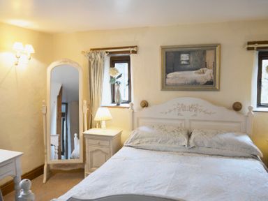 A bedroom with a bed a bedside table with lamp a standing mirror and two small windows at Bothy in Nenthall near Alston