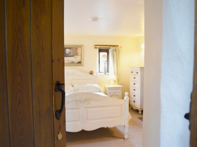 A bedroom with a white bed a bedside table with a lamp a chest of drawers and a small window at Bothy in Nenthall near Alston